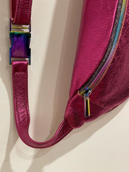 Close-up of metallic pink leather fanny pack with a colorful zipper pull on a light background
