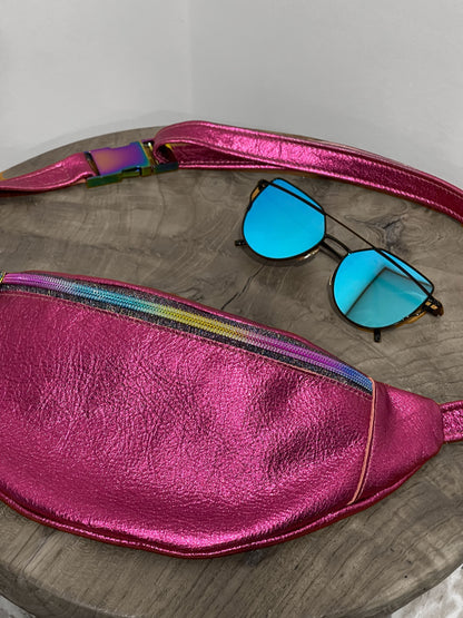 Pink metallic fanny pack with colorful strap and blue sunglasses on a wooden surface.