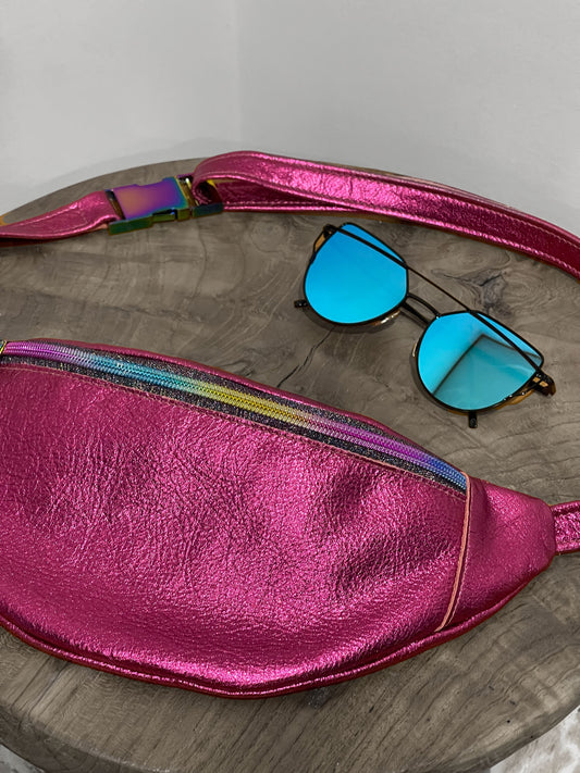 Pink metallic fanny pack with colorful strap and blue sunglasses on a wooden surface.