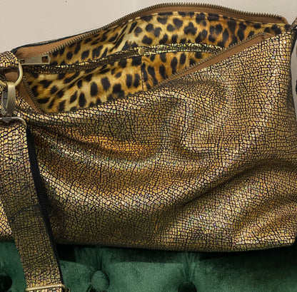 Gold textured handbag with leopard print interior on a green surface