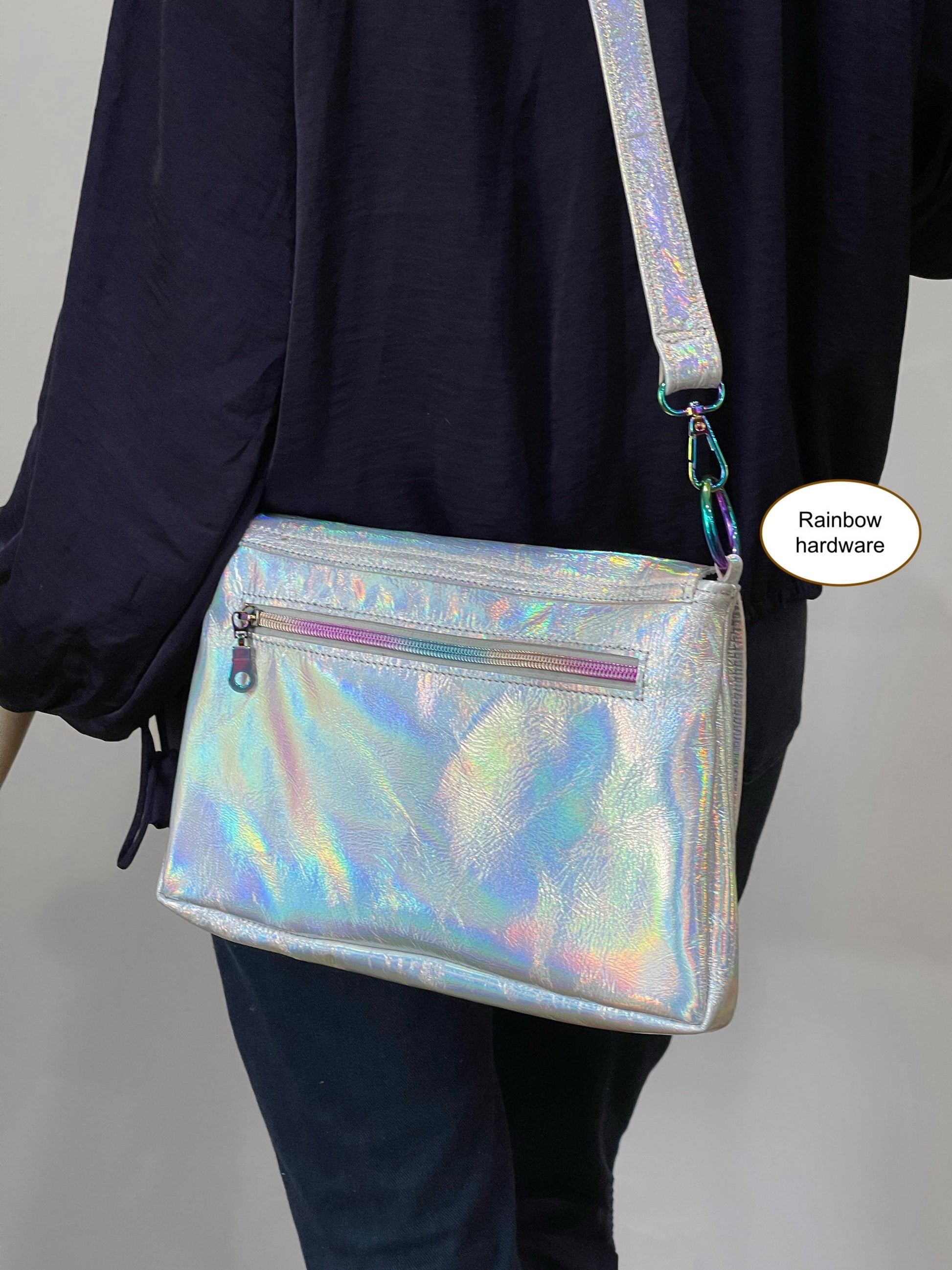 Holographic handbag with rainbow hardware worn by a person against a neutral background