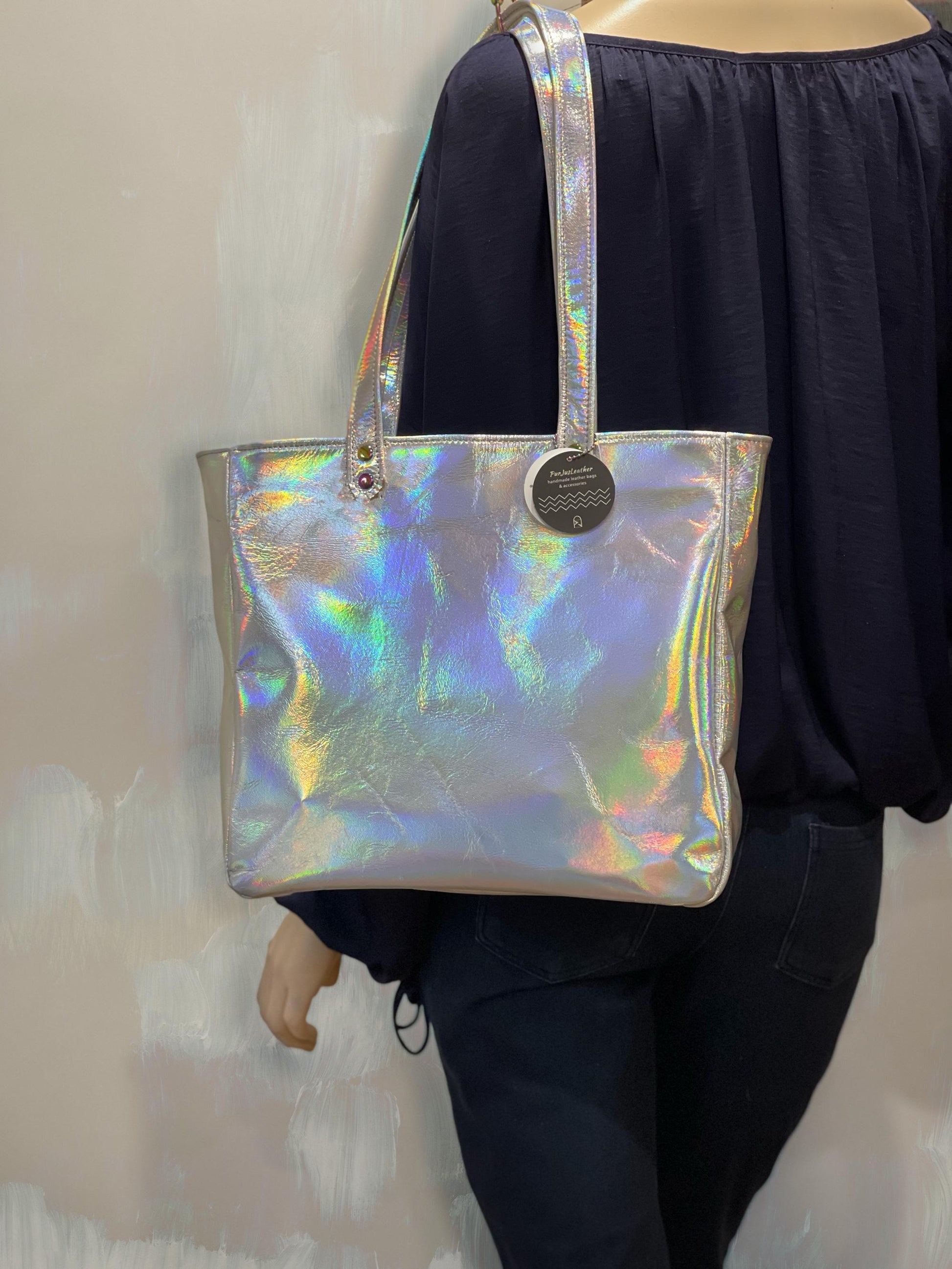 Holographic tote worn on a persons shoulder with large gap in straps for arms against a neutral background