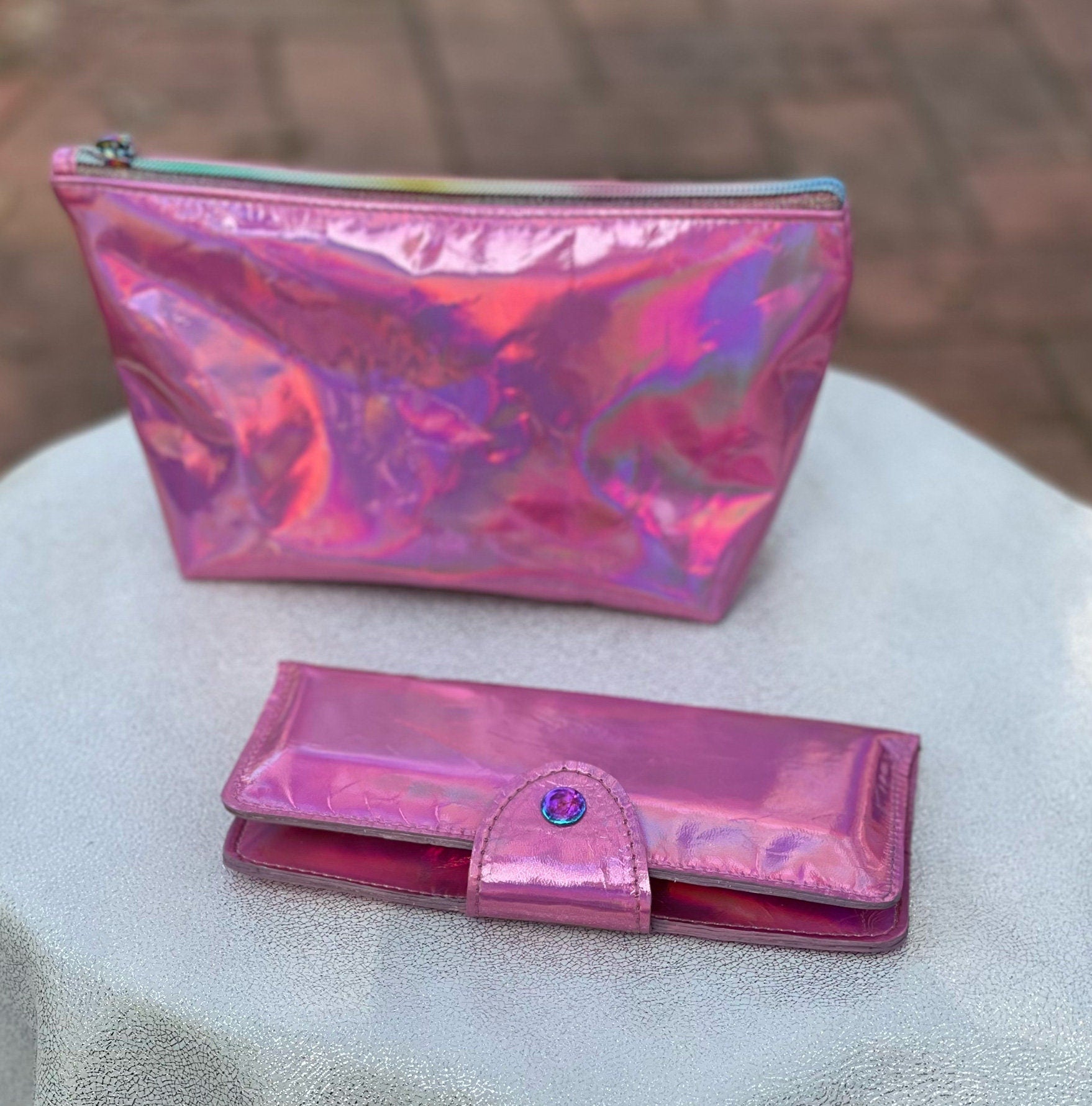 Pink iridescent pouch and wallet on a textured surface with a blurred background