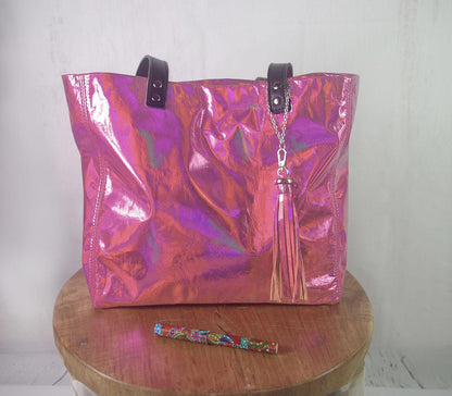 Holographic pink tote bag with a tassel on a wooden stool against a white wall.