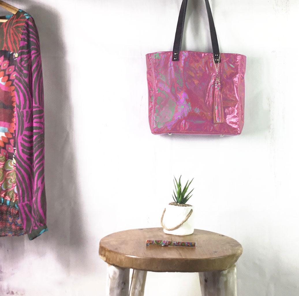 Pink patterned bag hanging on a white wall with a wooden stool and plant below.