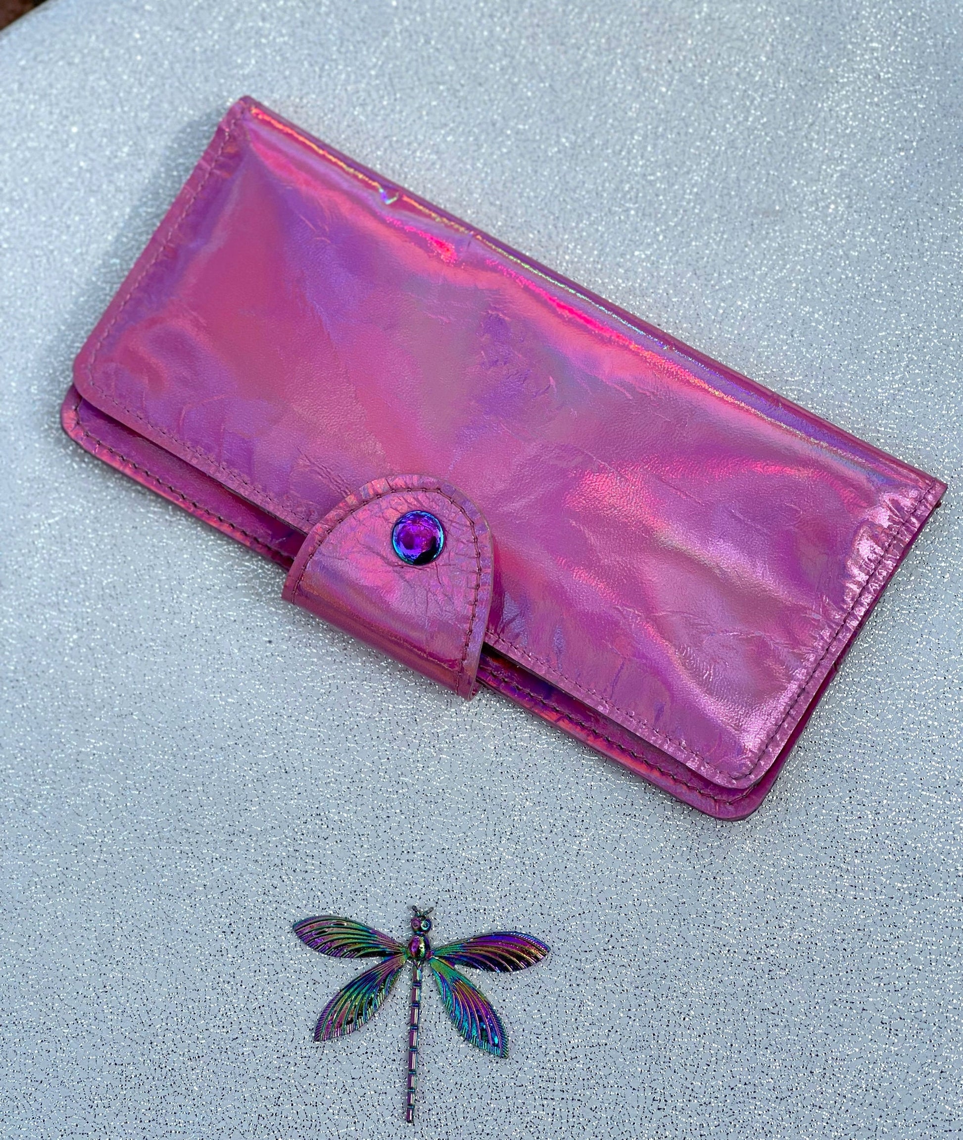Holographic pink wallet with a dragonfly charm on a light gray background