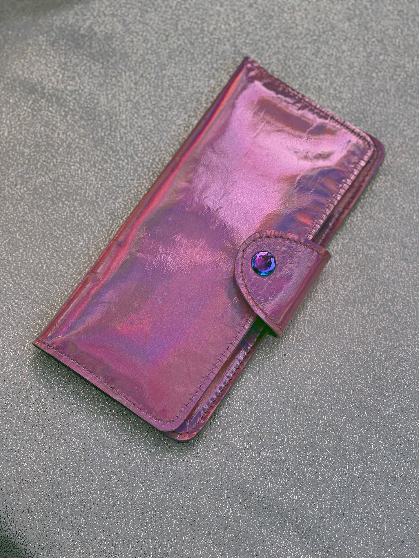 Closed Holographic pink wallet with rainbow hardware on a gray surface