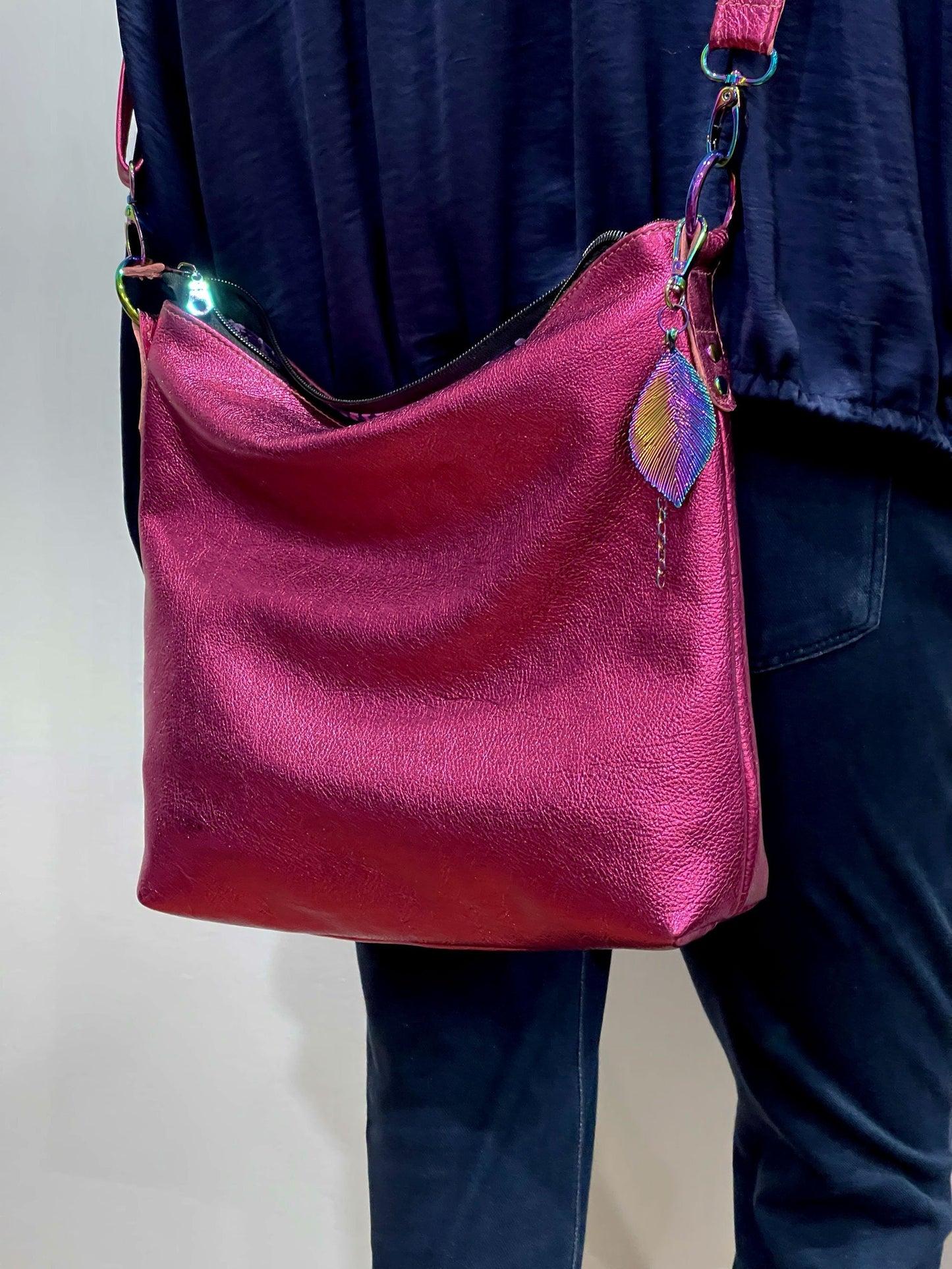 Pink handbag with colorful leaf charm worn by a person against a neutral background
