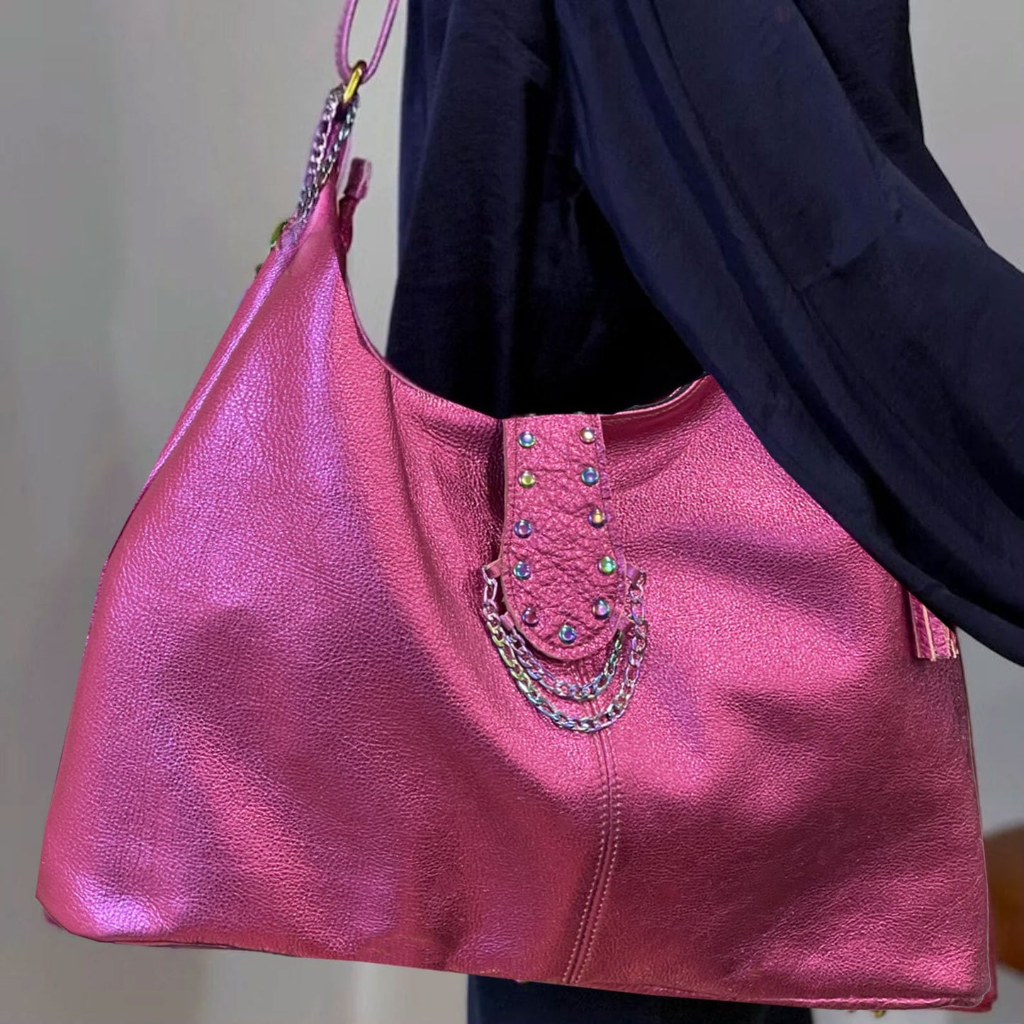 Pink handbag with decorative chain detail held by a person wearing a dark jacket.