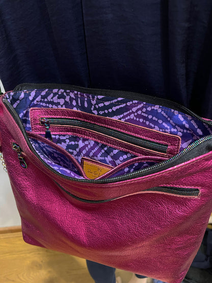 Pink metallic soft handbag with open zipper showing purple interior against a dark background