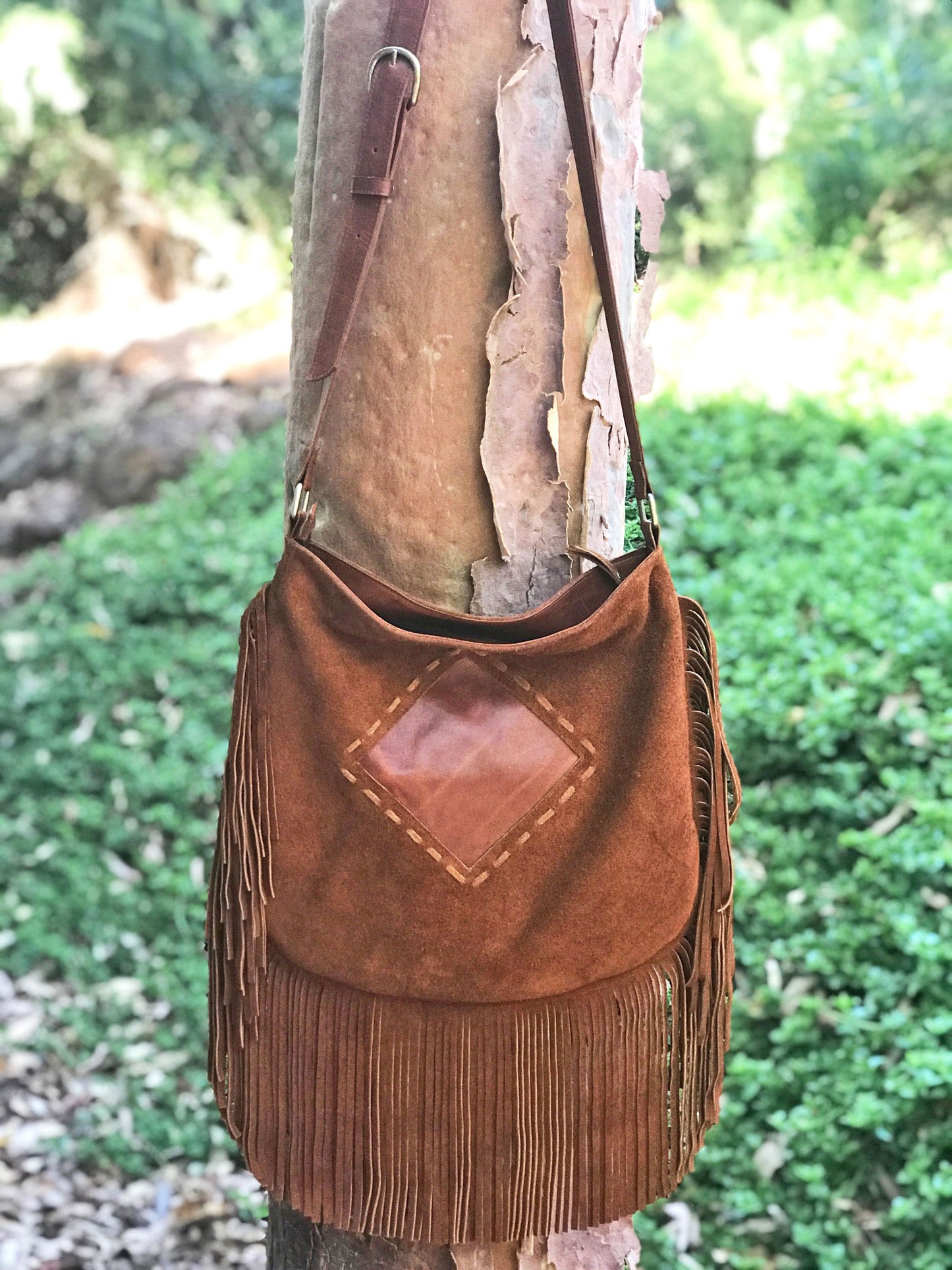 Brown suede handbag with fringe hanging on a tree trunk outdoors