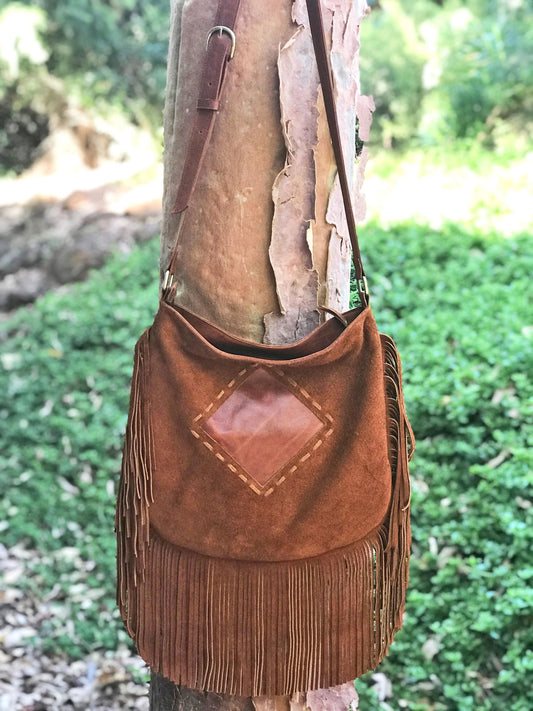 Brown suede handbag with fringe hanging on a tree trunk outdoors