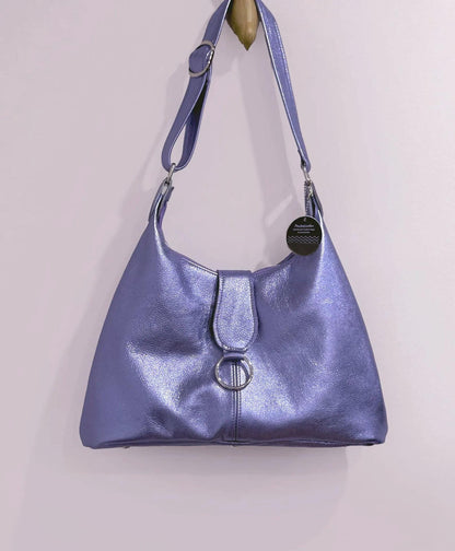 lilac handbag with a circular flap feature and adjustable wide strap on a light gray background