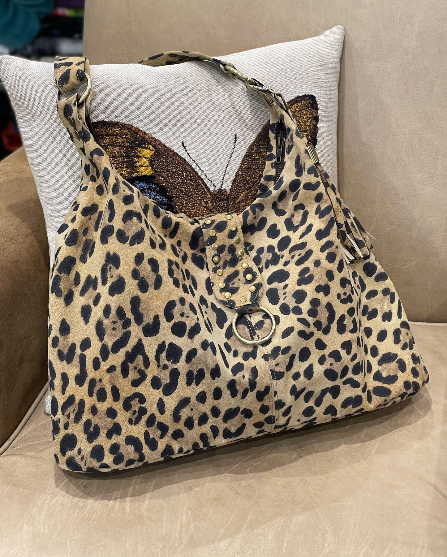 Leopard print handbag with O ring and riveted flap on a cushioned surface