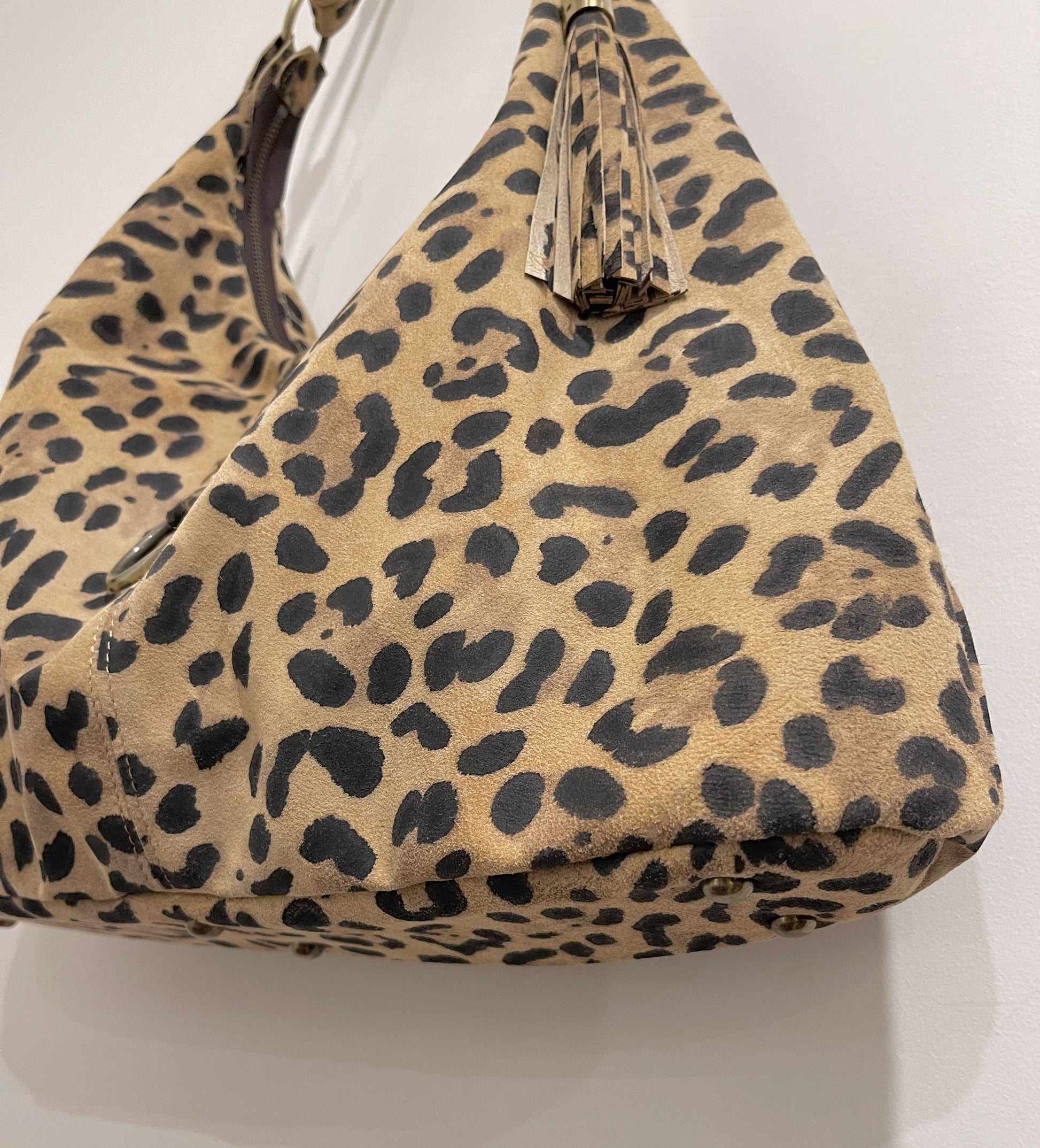 an edgy Leopard print suede handbag with tassel on a white background