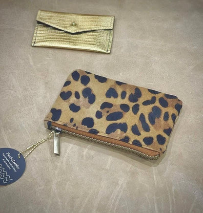Leopard print wallet with gold clutch and tag on a beige surface