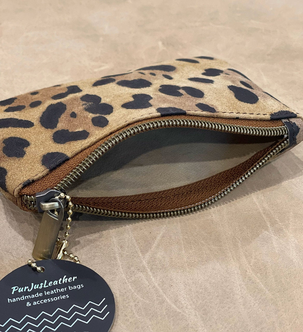 Leopard print pouch shown open with natural unlined suede inside with a visible brand tag on a beige surface
