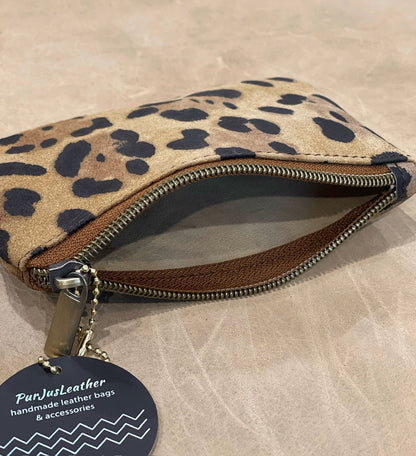 Leopard print pouch shown open with natural unlined suede inside with a visible brand tag on a beige surface