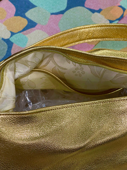 close up of a Gold handbag with floral lining and zipper closure set down into bag on a colorful patterned background