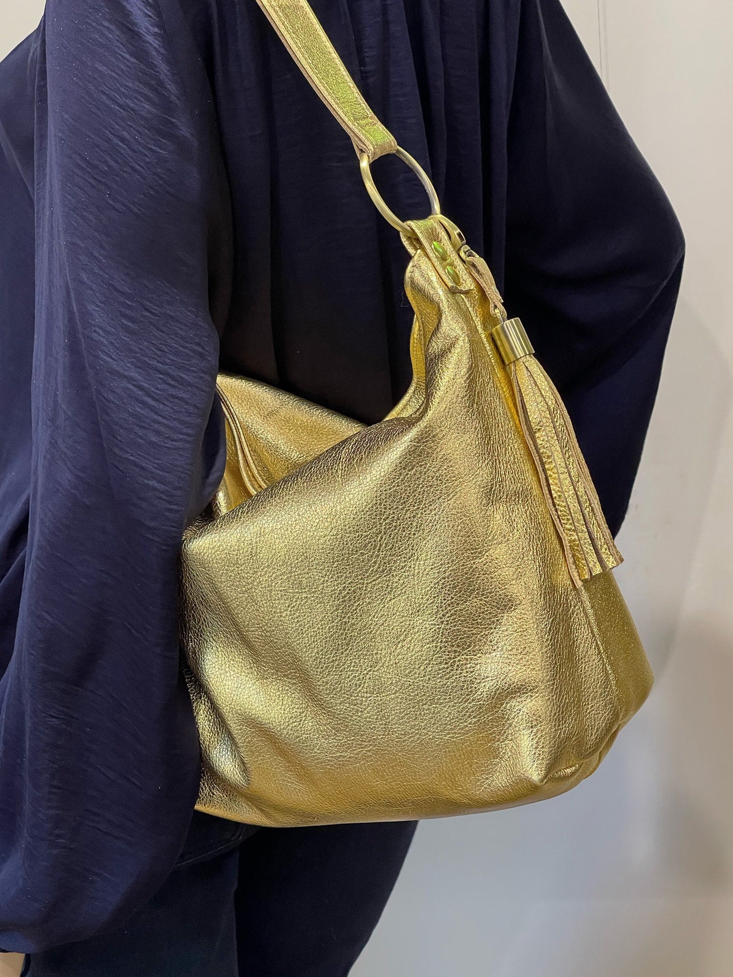 Gold handbag with matching gold tassel held by a person wearing a dark blue outfit.