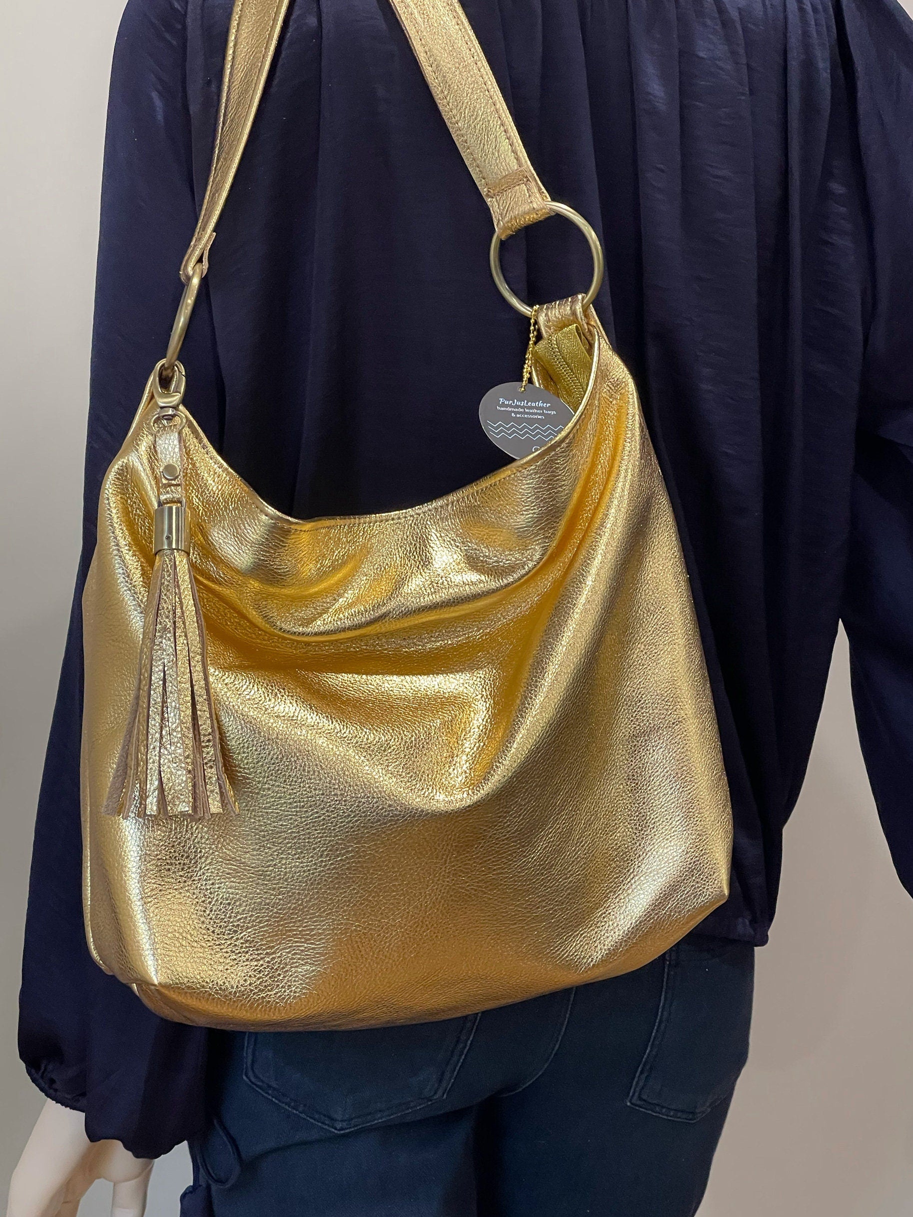 Gold metallic handbag with a visible brand tag, worn by a person in a dark outfit.