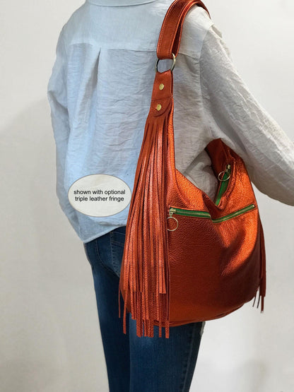 Orange leather handbag with fringes worn by a person on a plain background