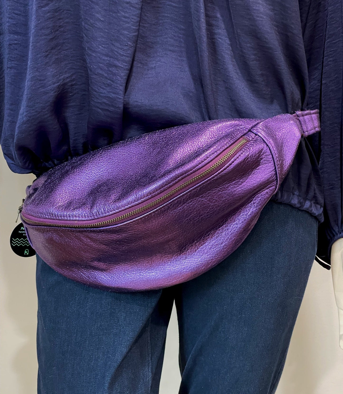 Person wearing a purple metallic fanny pack on a plain background