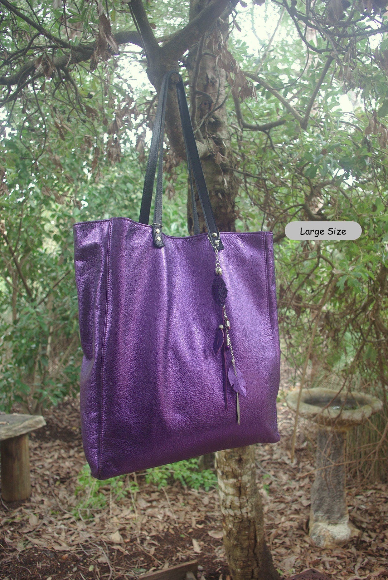Purple tote bag with black handles hanging from a tree in a forest setting
