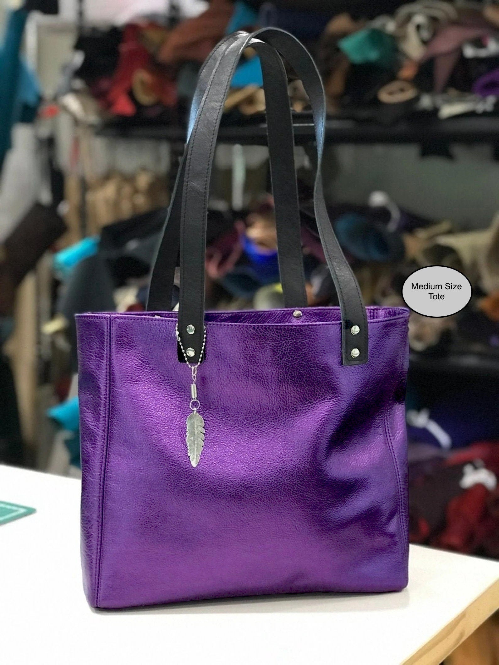 Metallic Purple Leather handbag with black handles on a white surface, magnet close. leaf charm