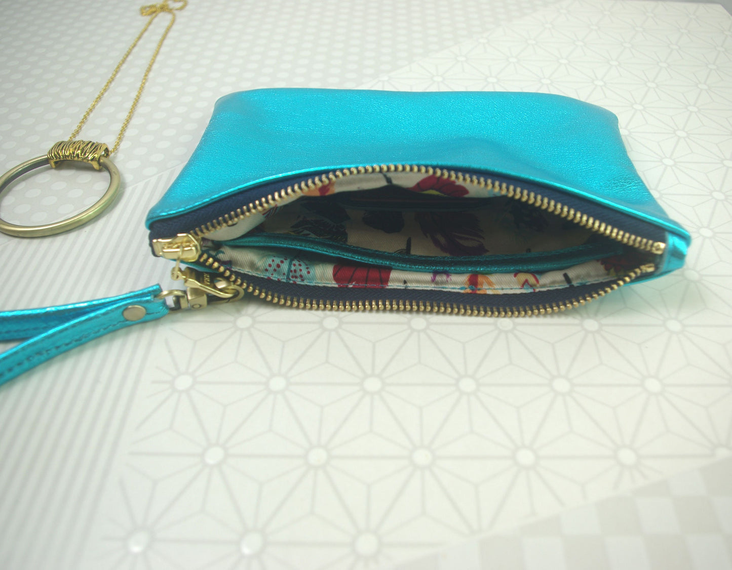 Turquoise Blue clutch with feather print interior slip pocket on a white textured background
