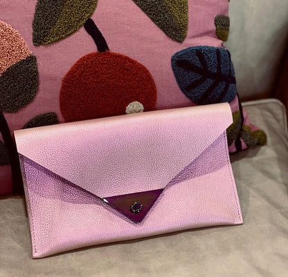 Pink envelope clutch with a decorative pillow in the background