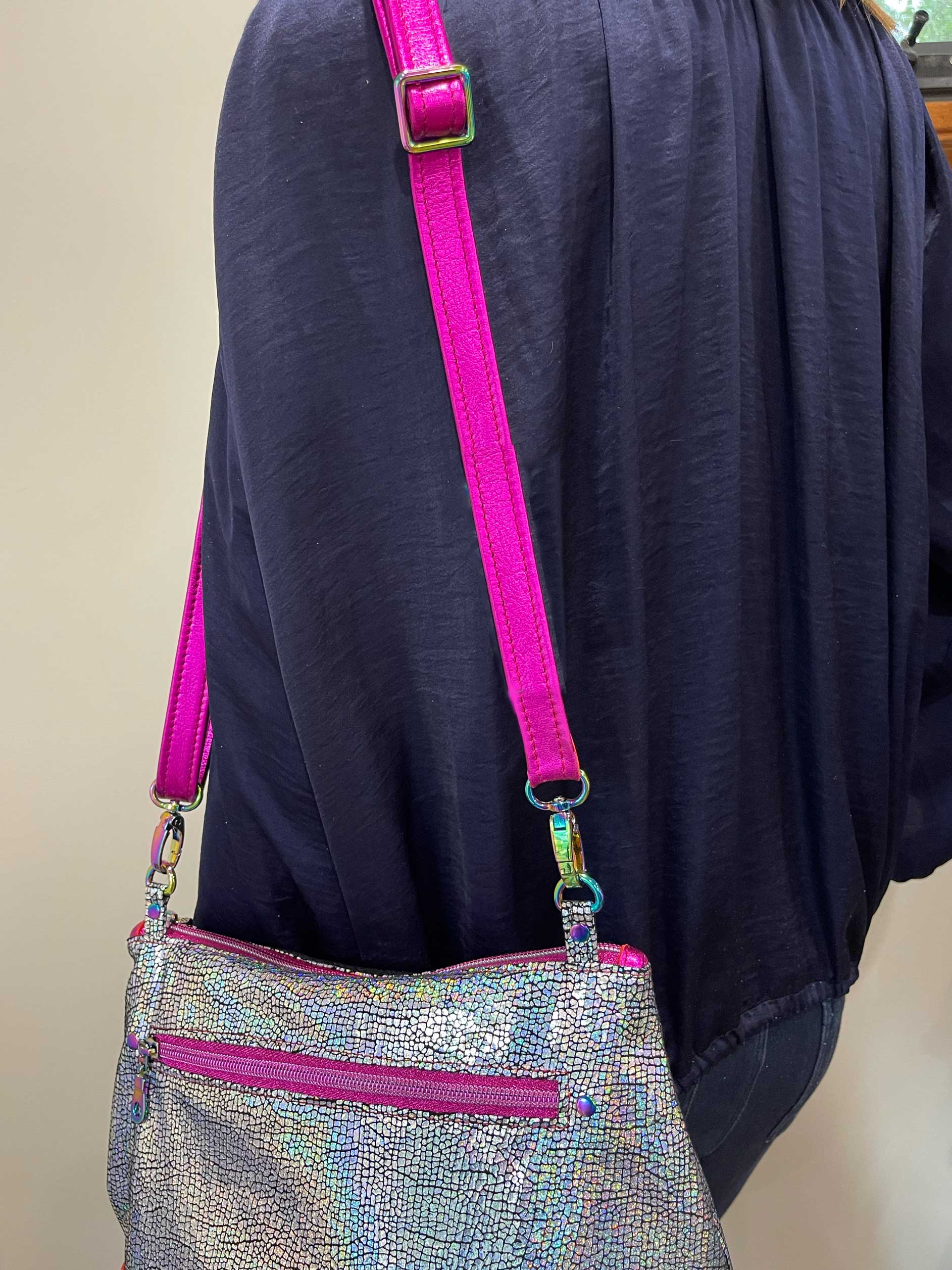 Silver handbag with pink strap and trim on a person wearing a dark blue garment.