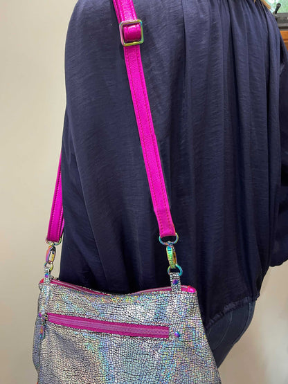 Silver handbag with pink strap and trim on a person wearing a dark blue garment.