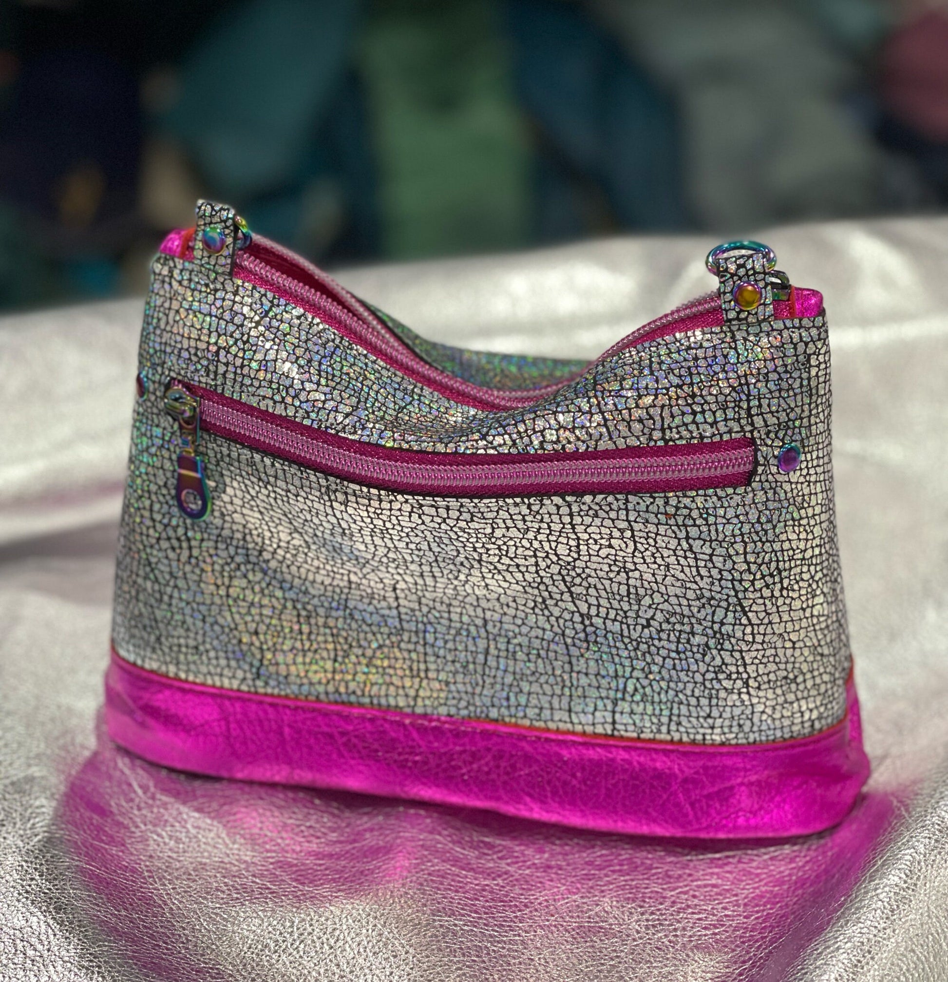 Silver textured pouch with pink zipper on a reflective surface