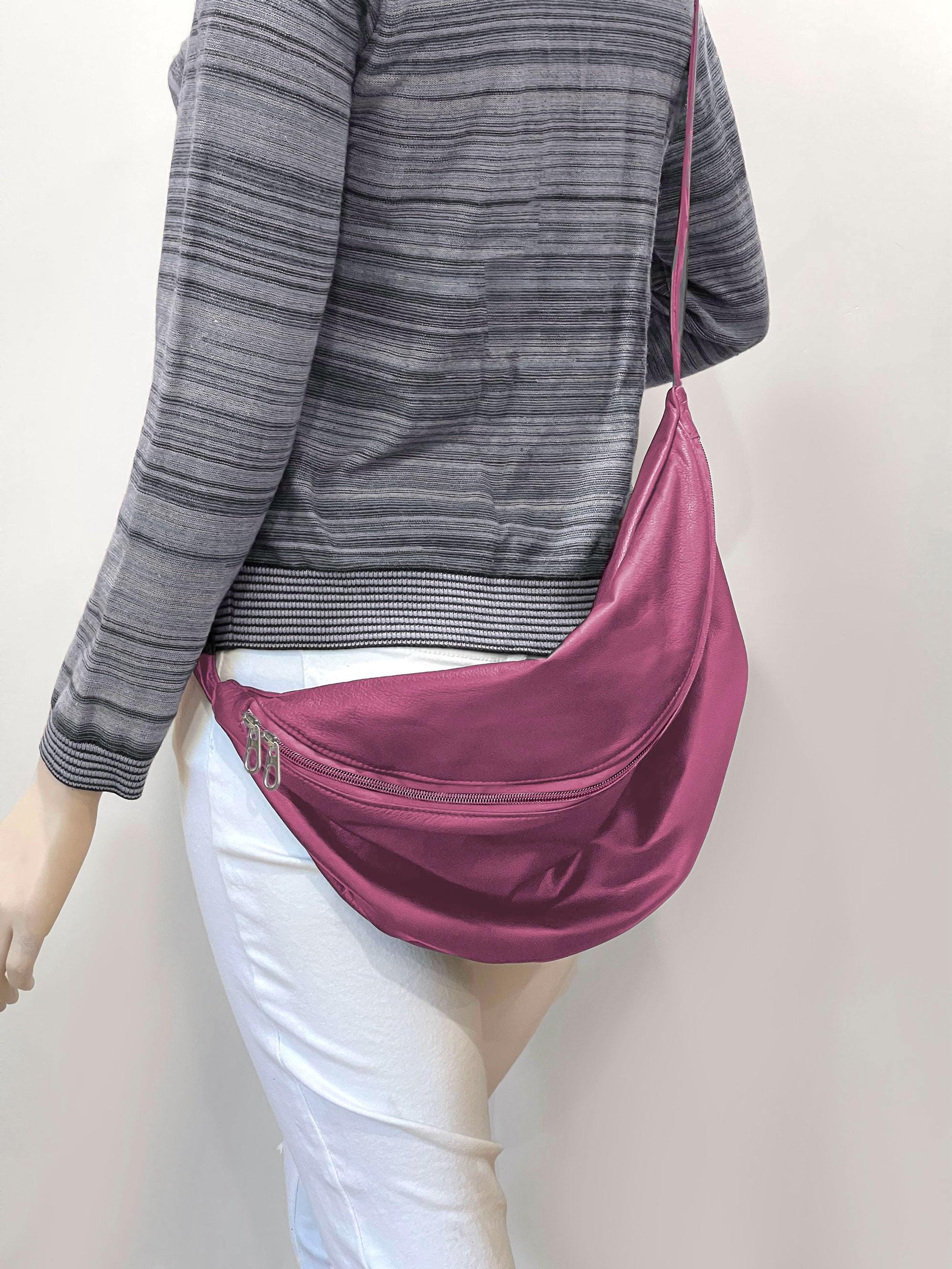 Person wearing a pink sling bag with double zipper opening over one shoulder against a plain background