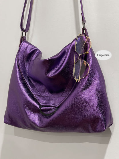 Purple handbag with flap close and large D ring and sunglasses hanging on edge on a light gray background