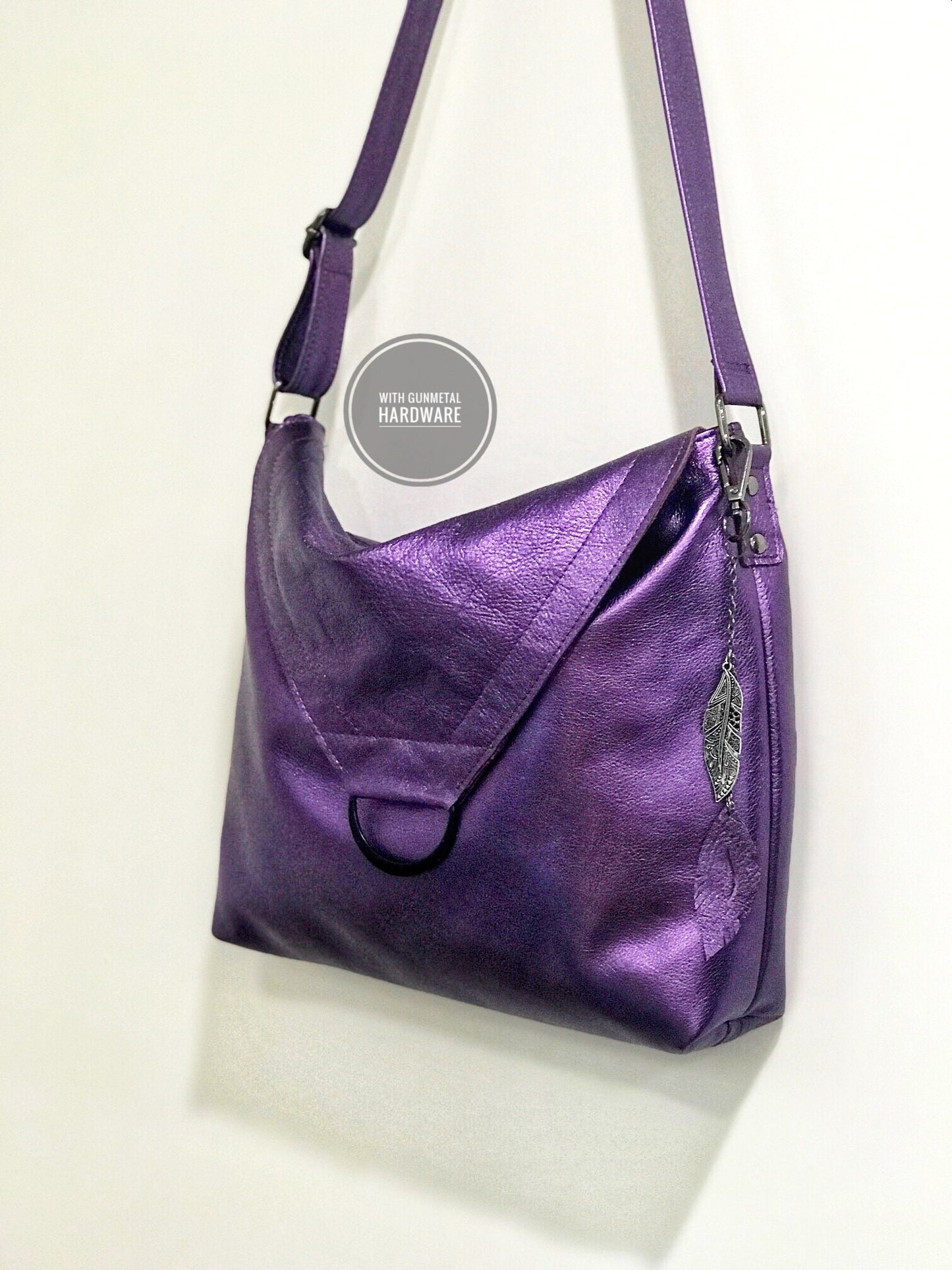 Side view of Purple metallic handbag with a leather and metal feather bag charm on a light background
