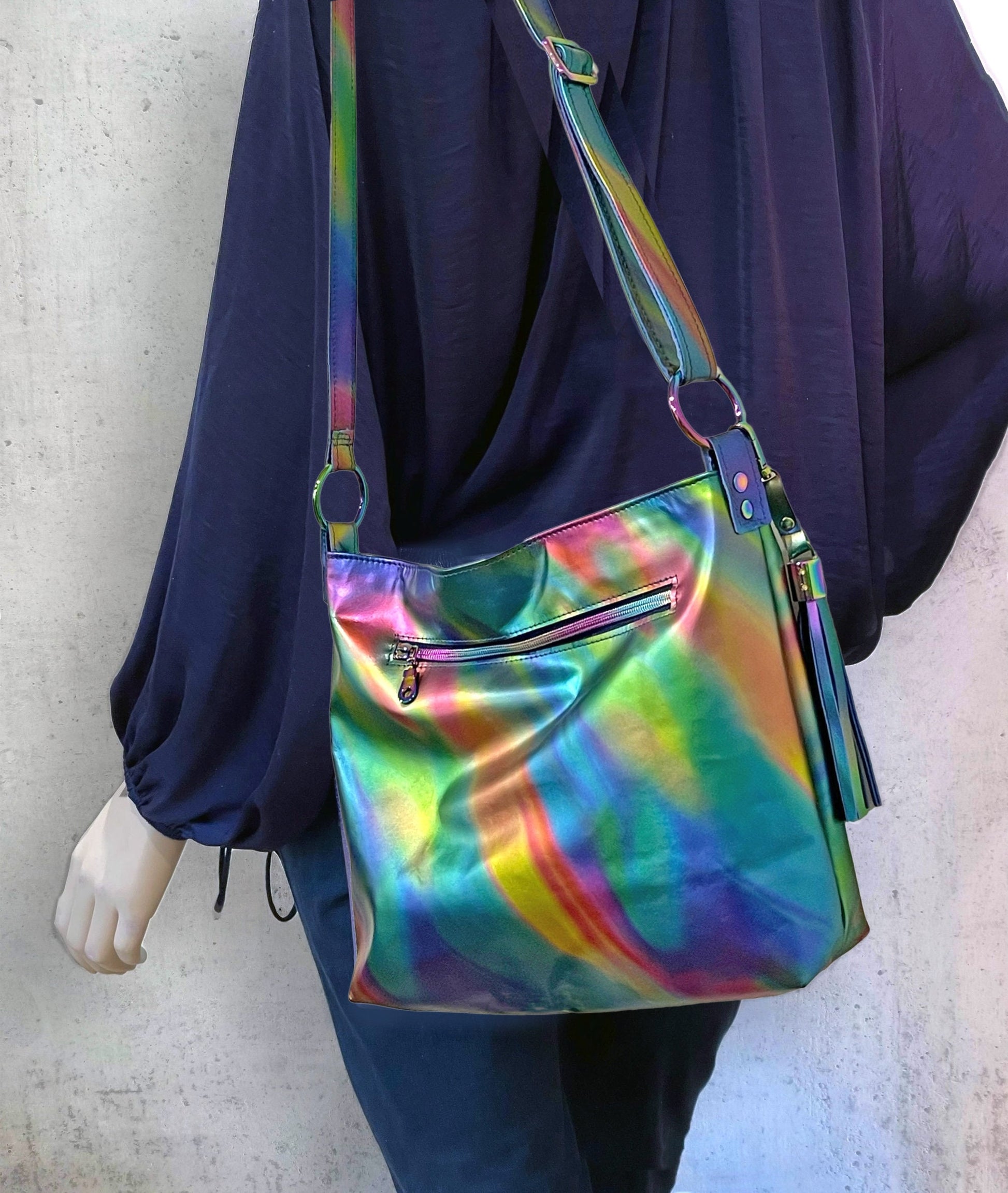 Multicolored handbag with a strap attached to rainbow metal O rings and showing an outside zipper pocket over shoulder against a neutral background