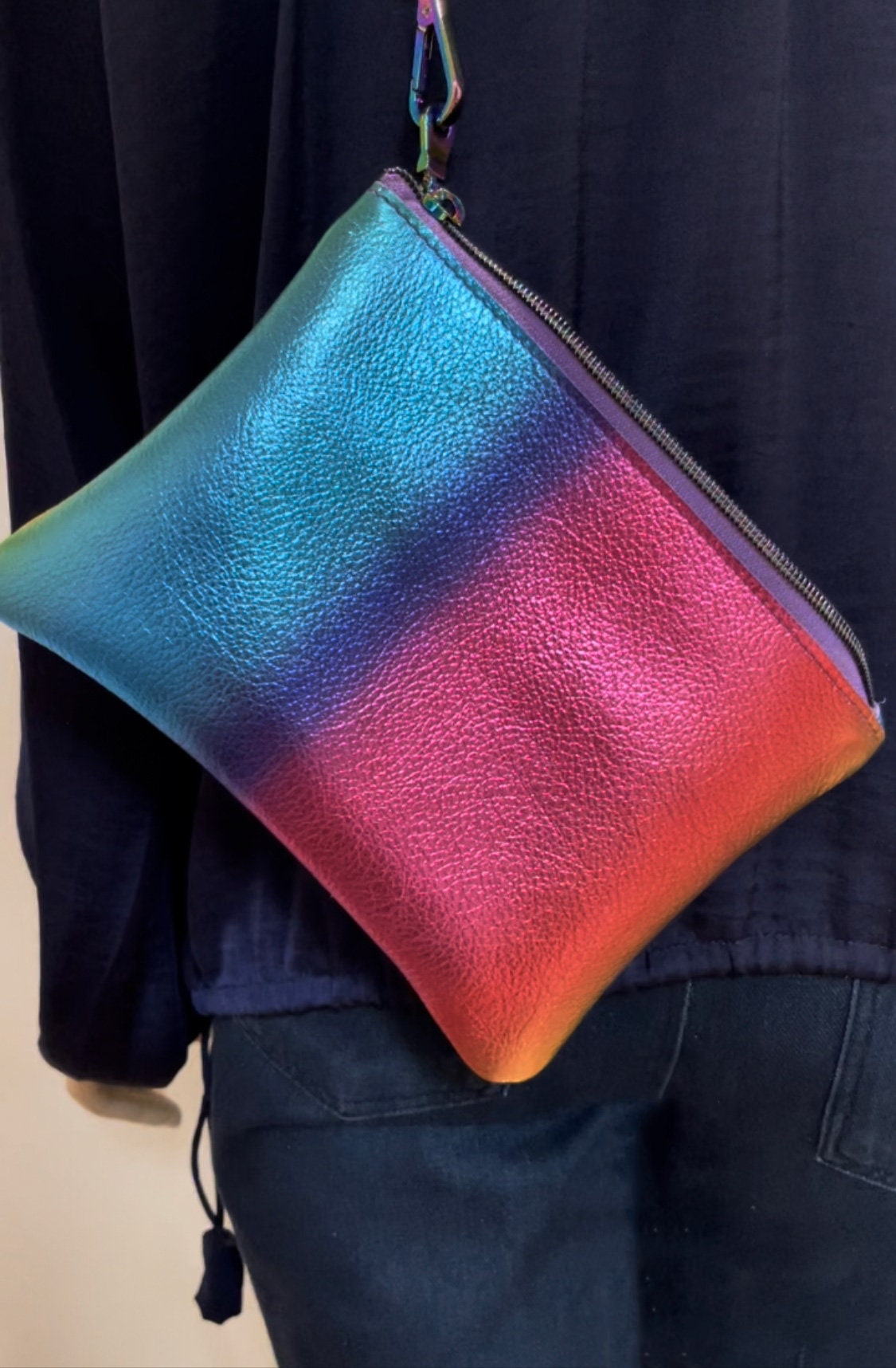 Gradient rainbow stripe blue to pink pouch held by a person wearing a dark jacket.
