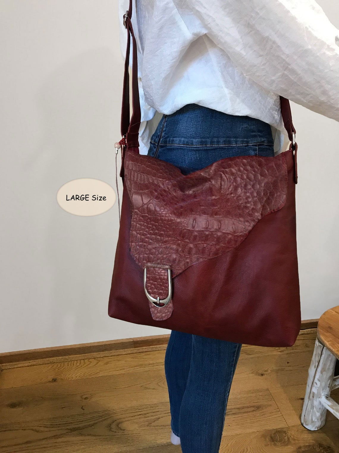 Person wearing a large burgundy leather bag with a croco embossed asymmetrical flap with a silver buckle