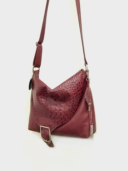 Maroon leather handbag with a textured pattern and bag charm on a white background