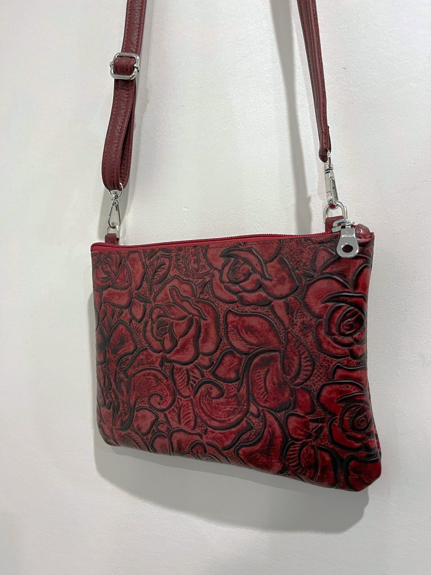 Red leather handbag with floral tooled pattern and narrow leather strap removable and adjustable on a white background
