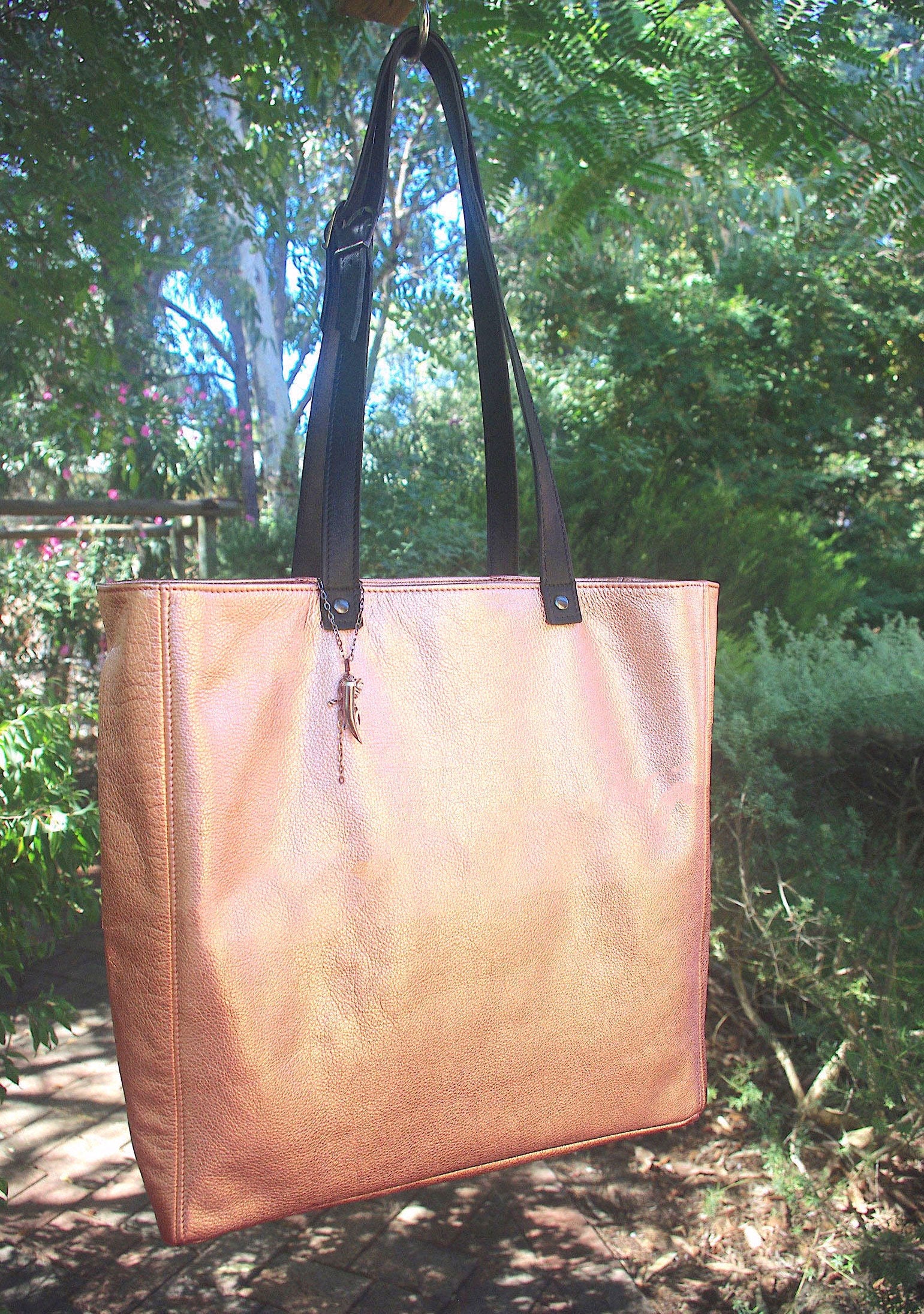 rose gold metallic leather tote bag with black handles against a natural background