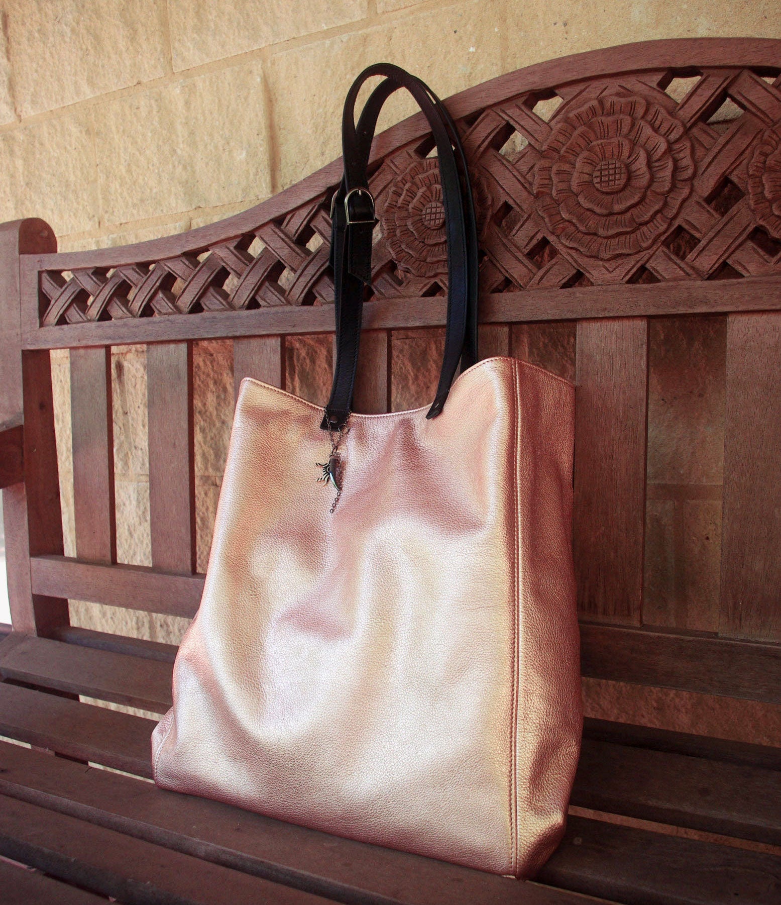 rose gold tote bag with black straps on a wooden bench