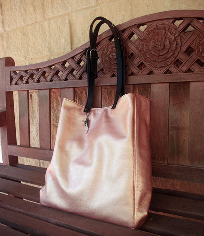 rose gold tote bag with black straps on a wooden bench