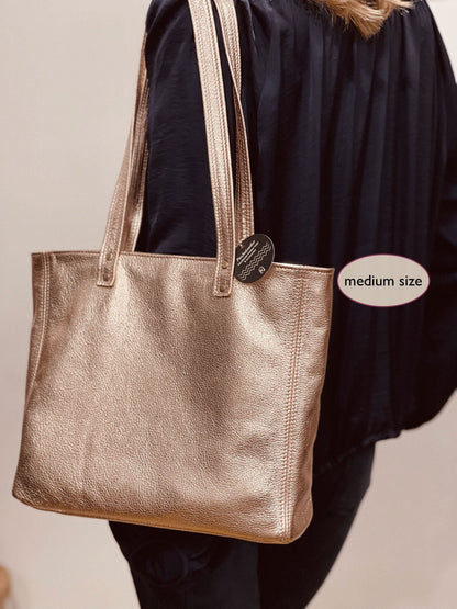 Rose gold metallic leather medium size  tote bag held by a person with a design label attached