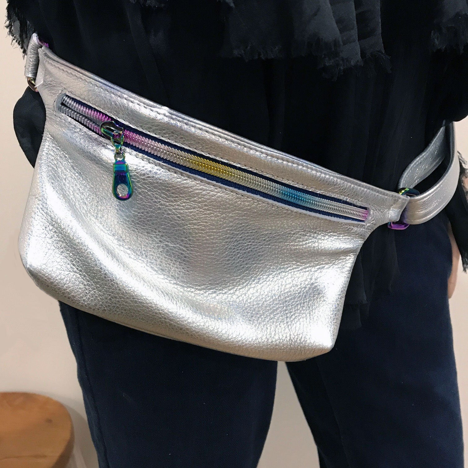 Silver fanny pack with a colorful zipper worn by a person against a neutral background
