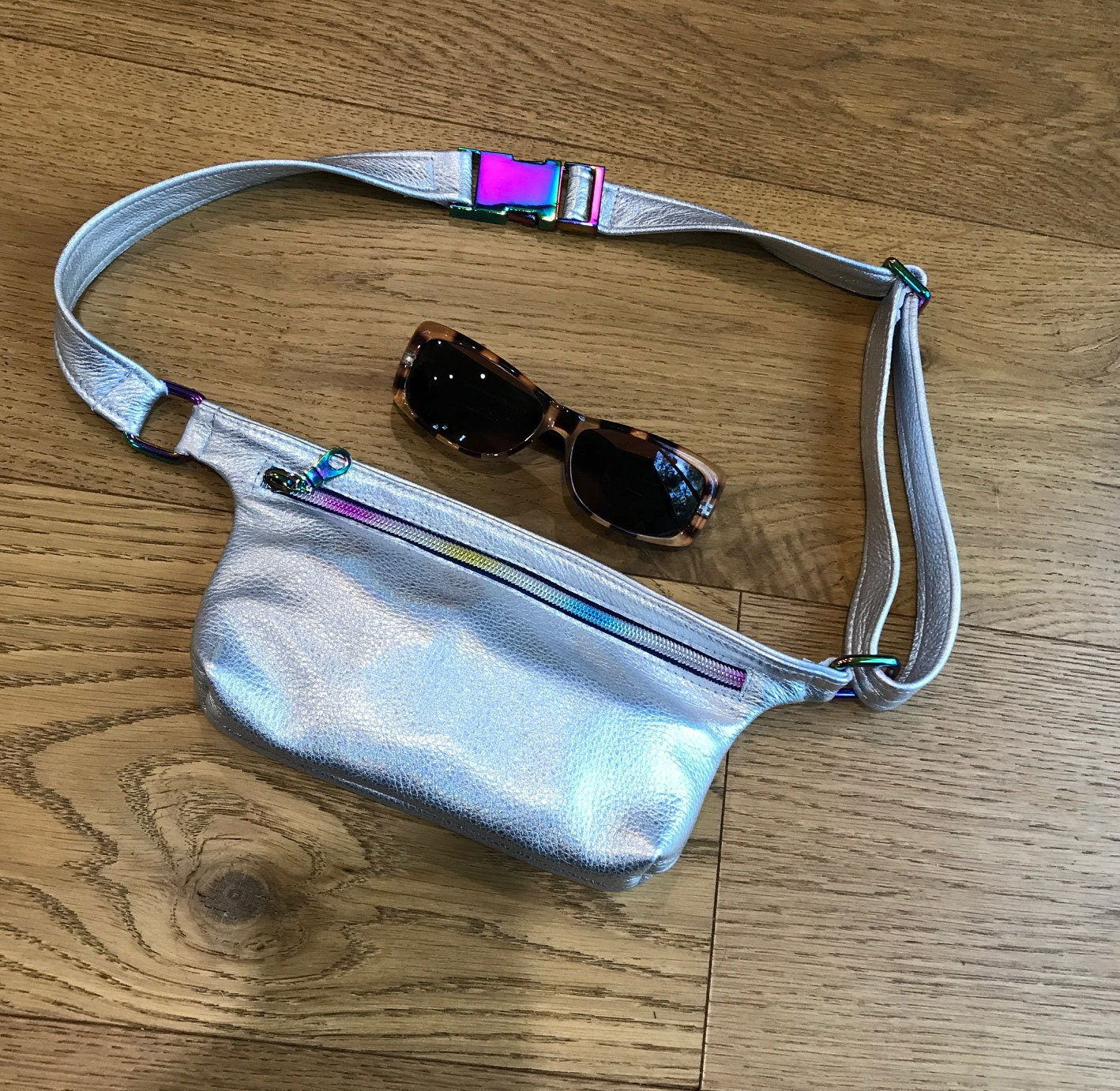 Silver reflective fanny pack with sunglasses on a wooden surface