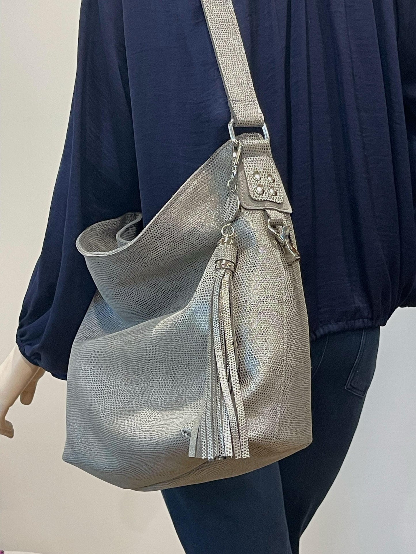 Person wearing a pearlised silver handbag with tassels on a plain background