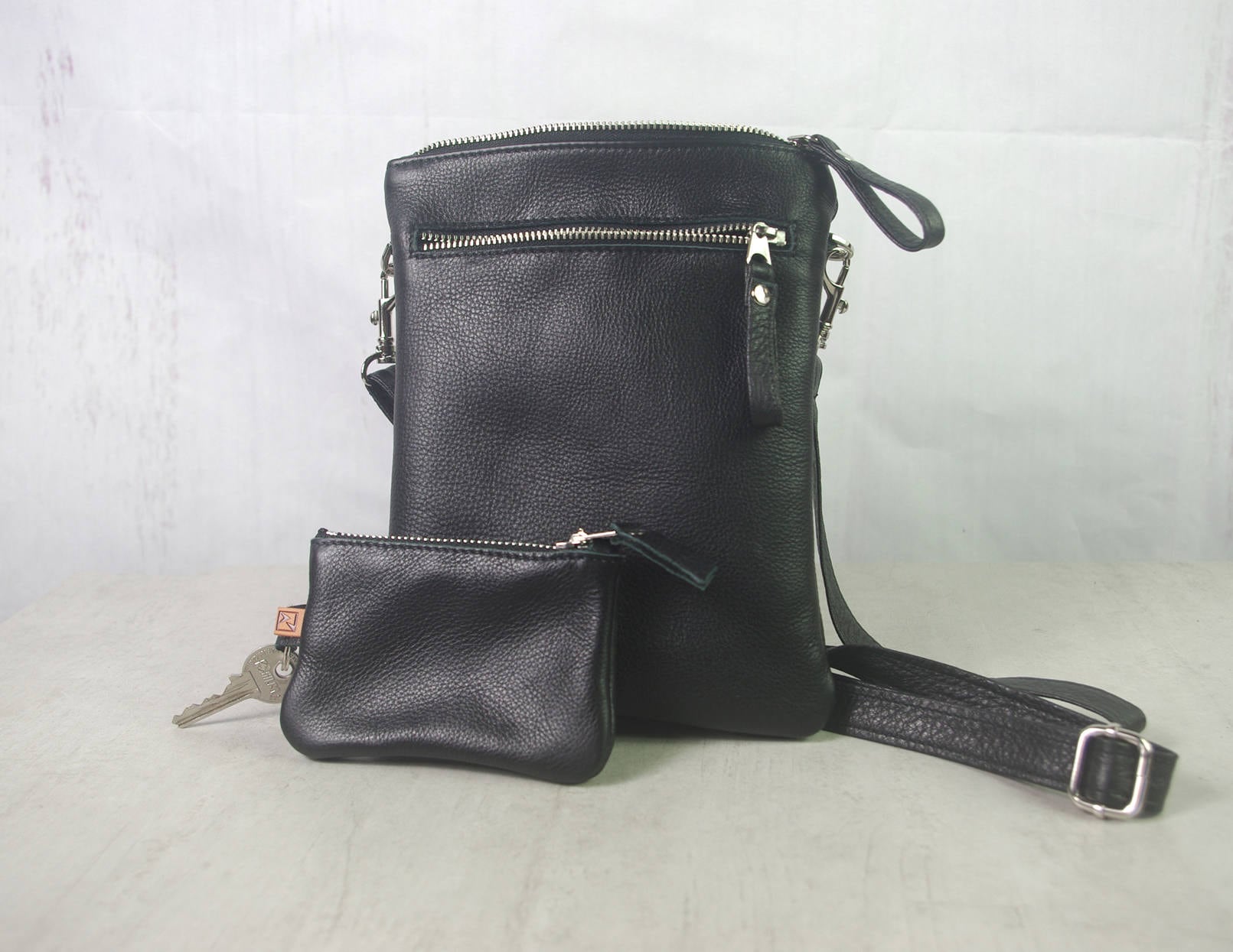 Black leather crossbody bag with matching pouch on a light gray background